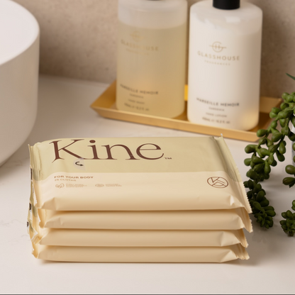 Stack of Kine  flushable wipes on a bathroom counter with bottles in the background. 100% plant-based wipes. Biodegradable flushable wipes. 