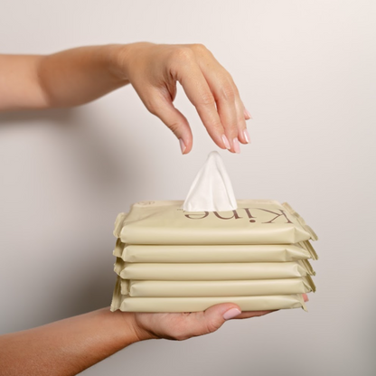 Hand holding a stack of Kine flushable wipes with a tissue being pulled out. Flushable intimate wipes, alcohol free wipes, biodegradable wipes, hypoallergenic wipes. Shop online now.