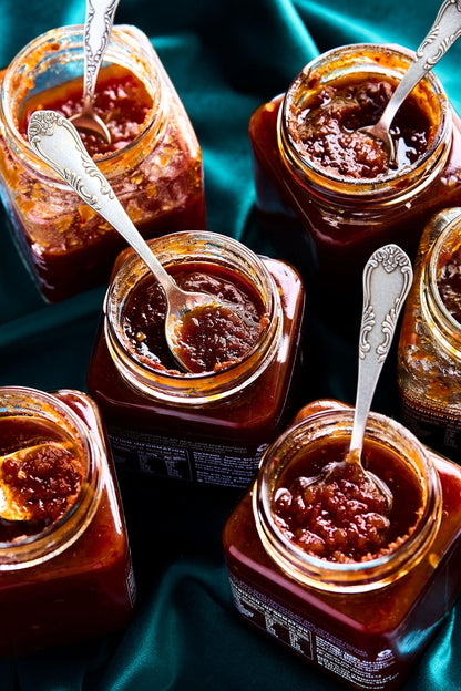 Jars of jam with spoons on a green fabric background
