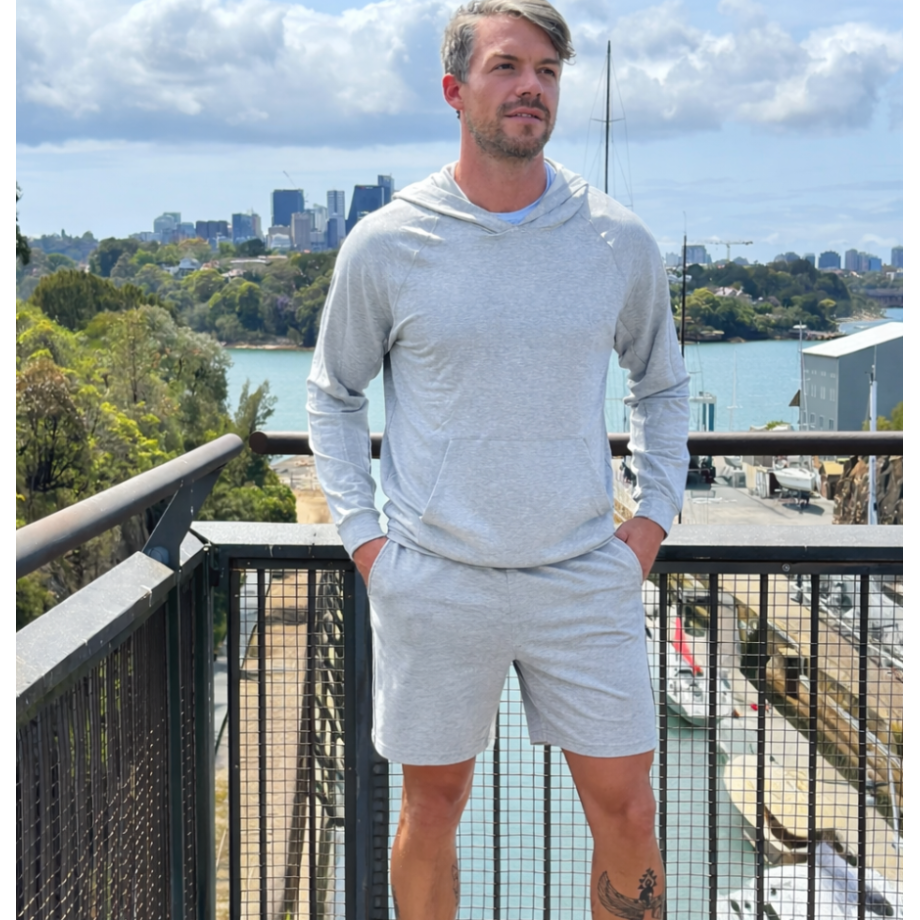 Man in gray hoodie and shorts standing on a balcony with a cityscape in the background