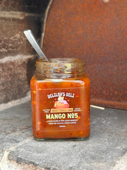 Jar of Delilah's Deli Mango No.5 sweet chilli jam with a spoon on a rustic surface.